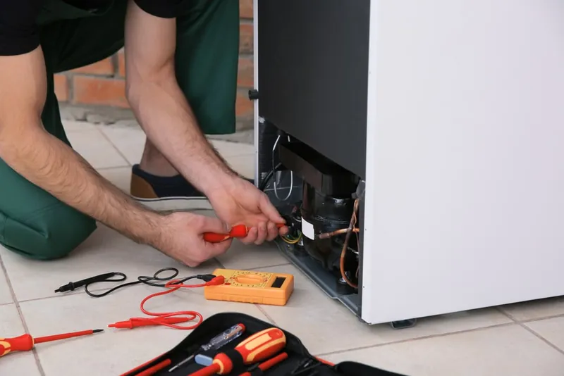 Technician using a multimeter to test the wiring at the back of a refrigerator