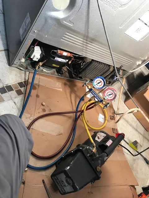 Manifold gauge set and vacuum pump connected to the sealed system of a refrigerator during compressor service