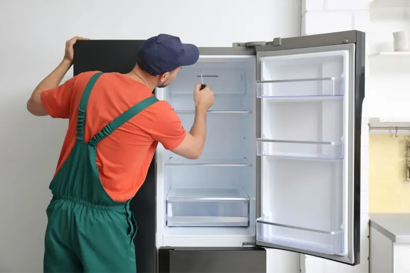 Technician checking the inside of an open refrigerator with a screwdriver